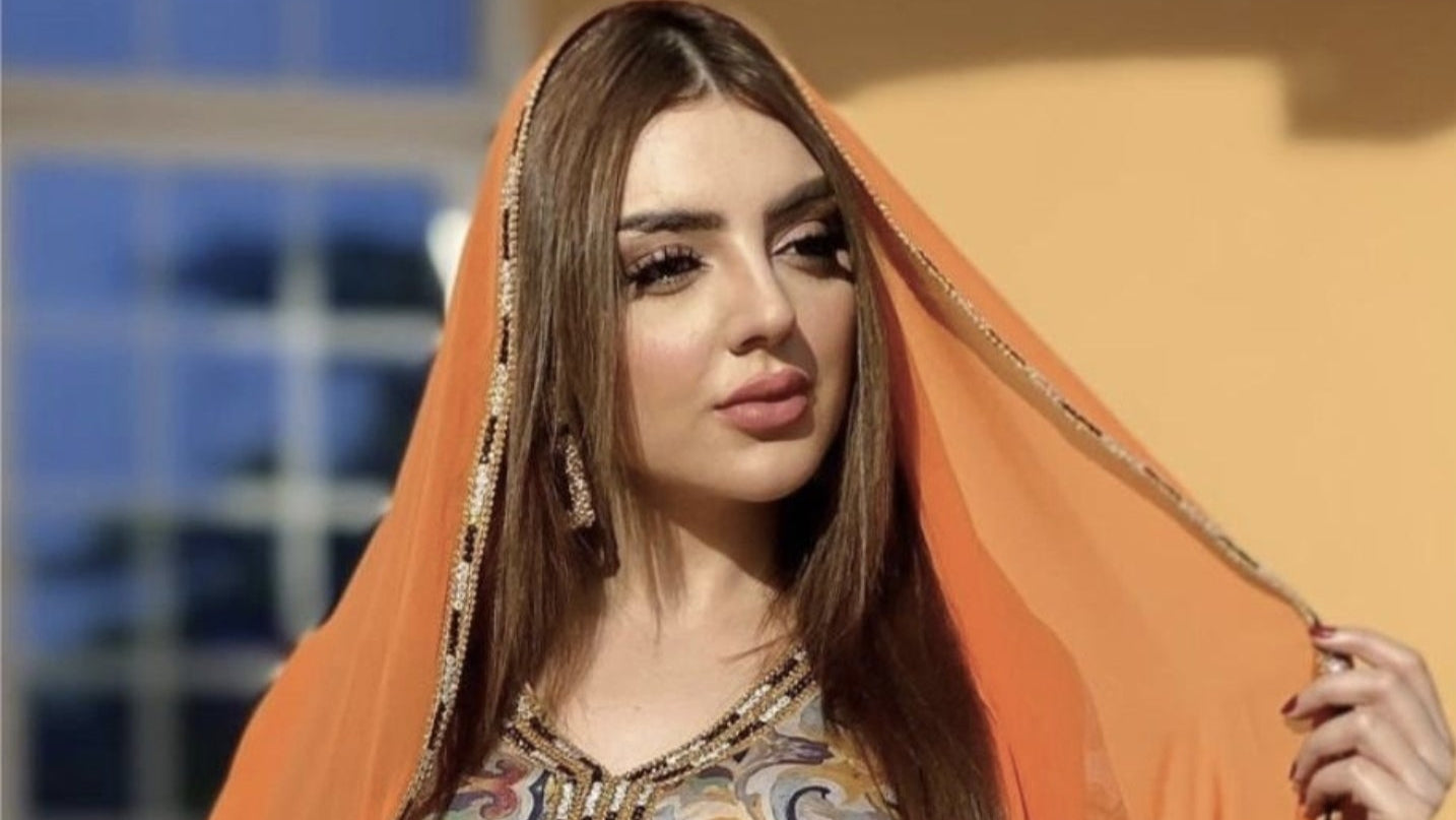 Woman wearing a patterned dress with an orange dupatta against a blurred background
