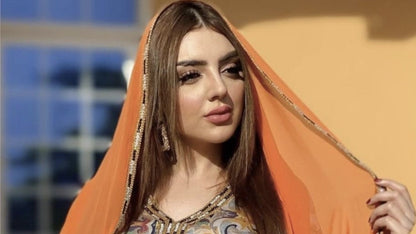 Woman wearing a patterned dress with an orange dupatta against a blurred background