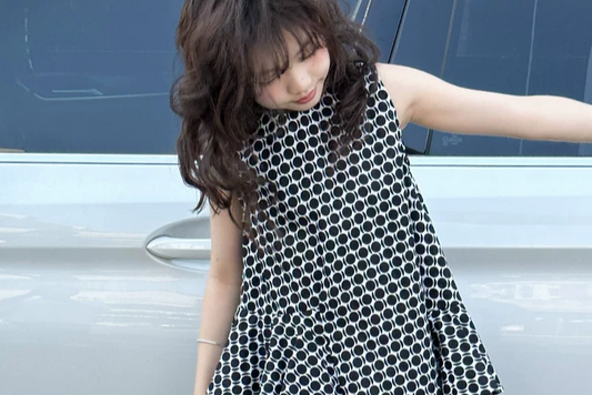 Girl wearing a black and white patterned dress standing next to a car.